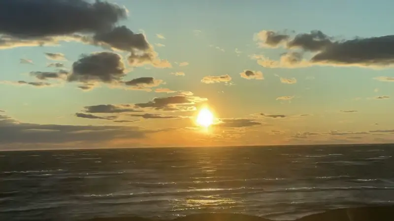 Ocean at sunset with clouds floating through the sky.